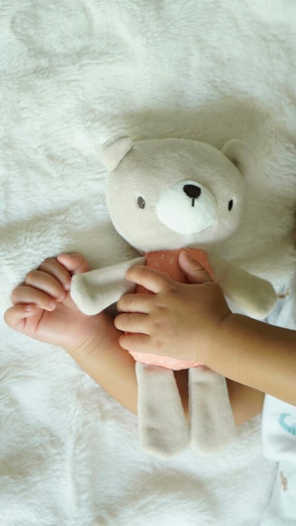 A child's hands gently hold a plush teddy bear on a soft white blanket, depicting comfort and innocence.